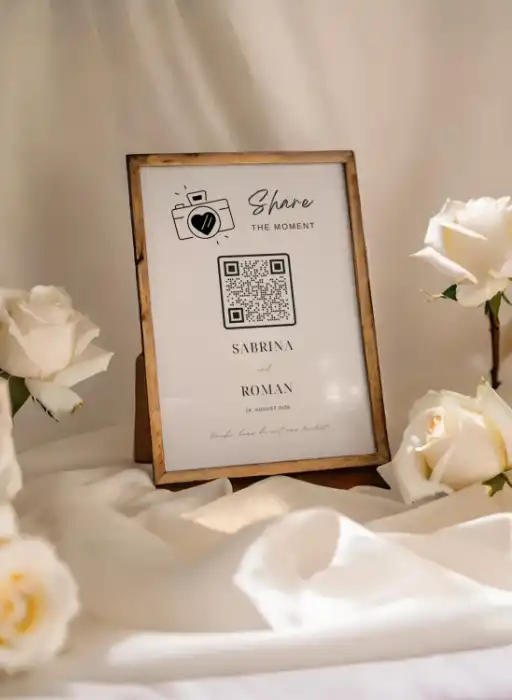 Framed wedding QR code sign for collecting photos from the guest book, surrounded by white roses.