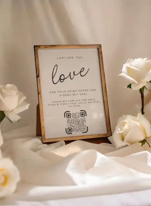 Wedding QR code sign for photo sharing, framed by roses, enhances digital guest book experience.